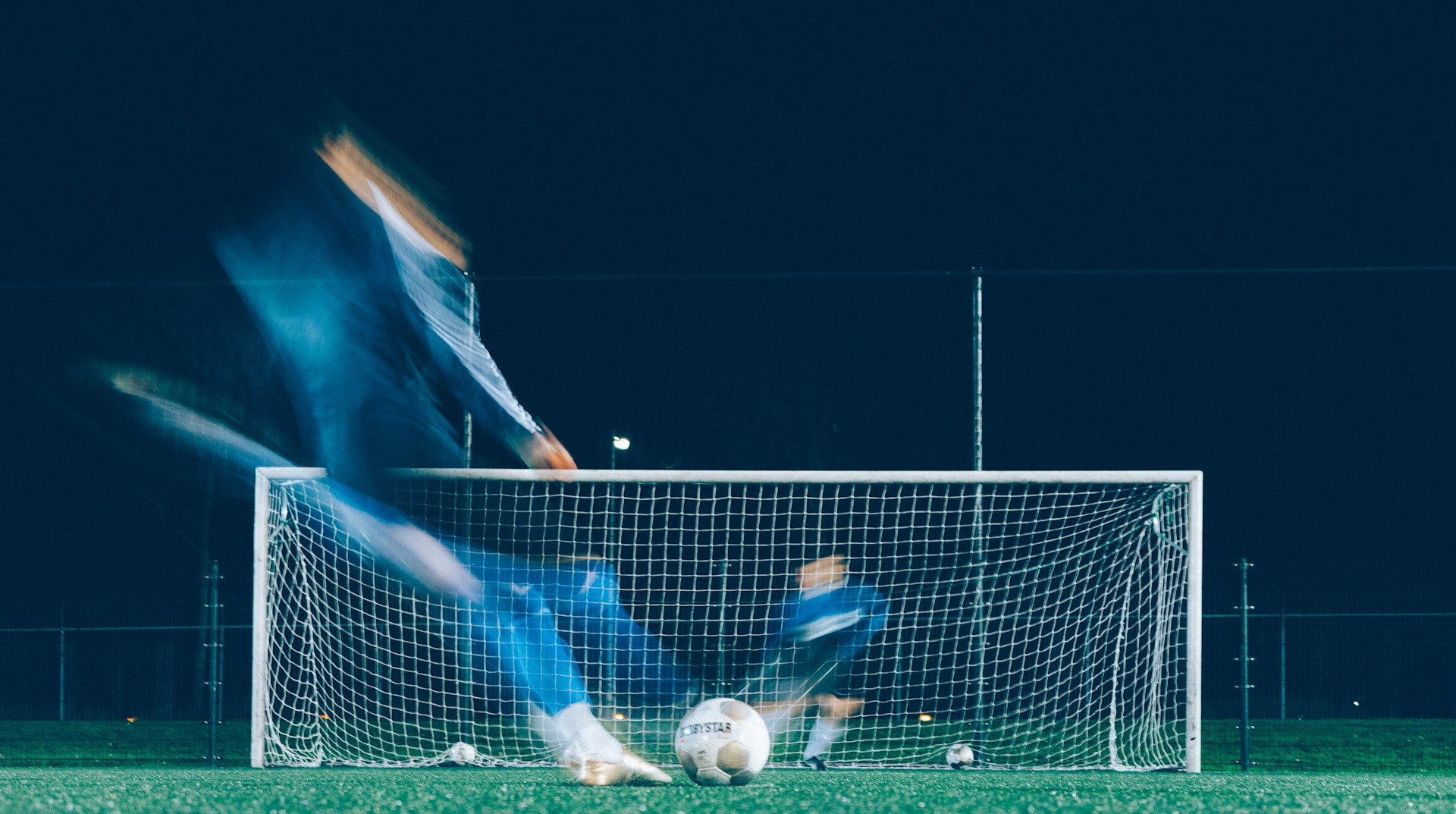 Zeitrafferfoto von zwei Fußballspielern, von denen ein Spieler einen Ball ins Tor schießt.