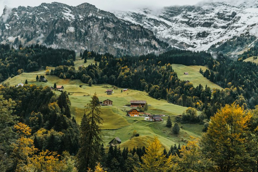 Schweizer Flagge weht auf einem Felsen, mit Blick auf eine grüne, hügelige Landschaft unter einem leicht bewölkten Himmel