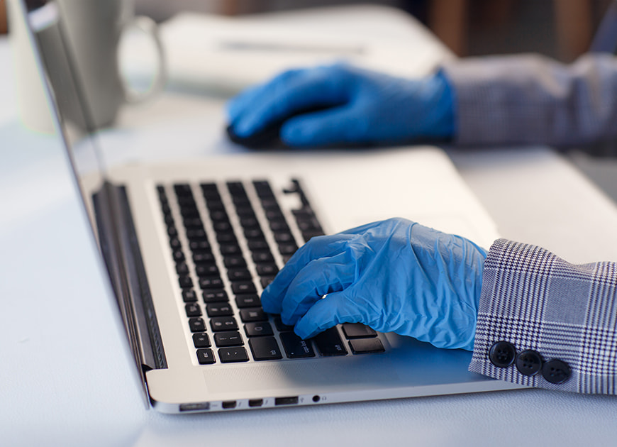 Person mit Handschuhen tippt auf einer Laptop-Tastatur.